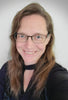 A woman with long brown hair and glasses smiles warmly at the camera in a black top against a light background, reflecting her passion for personal growth and the Guardian Tarot by Schiffer Publishing, Ltd.