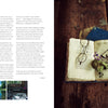 A pair of glasses, a violet flower, and leaves rest on an open book beside Schiffer Publishing, Ltd.'s The Herbarium of Fabric Flowers—an ideal source for inspiring rustic, vintage herbarium fabric projects.