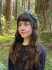 A woman with long brown hair and a leafy flower crown stands in a lush forest, reflecting the mystical spirit of The Animystic Tarot by Schiffer Publishing, Ltd.