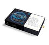 A partially open black box labeled "The Law of One Contemplation Deck" by Schiffer Publishing, Ltd. displays a cosmic blue design, a card with Ra quotations, and a gold ribbon tab for easy access.