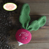 The Crochet Your Veggies Amigurumi Kit Radish by Schiffer Publishing, Ltd. features a smiling crocheted radish with two green leaves on a wooden surface beside spilled soil. The kit includes everything needed to make one radish.