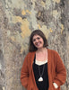 A woman with short brown hair and an orange cardigan smiles by a tree trunk—capturing a scene perfect for "The World in Me" by Schiffer Publishing, Ltd.