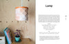A wooden table with books and a small purple potted plant sits by a wood-paneled wall. Above, the Bark Craft lamp by Schiffer Publishing, Ltd. hangs from the ceiling, its birch bark weaving and leather trim adding charm to the cozy space.