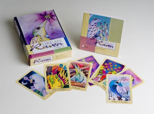 The Dream Raven Tarot by Schiffer Publishing, Ltd. is shown spread out with its vibrant box and guidebook, featuring illustrated ravens in bold, symbolic scenes.